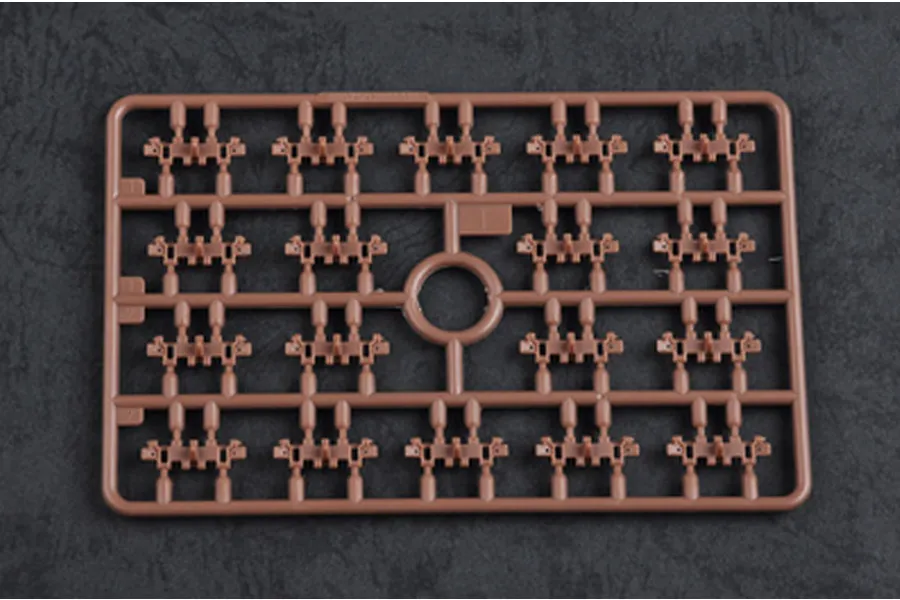 A brown plastic model kit sprue containing multiple small tank track link components on a dark textured background.