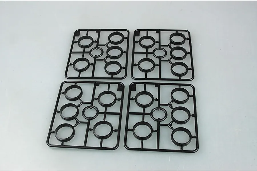 Four identical black plastic model kit sprues containing circular tank wheel parts arranged on a light grey background.