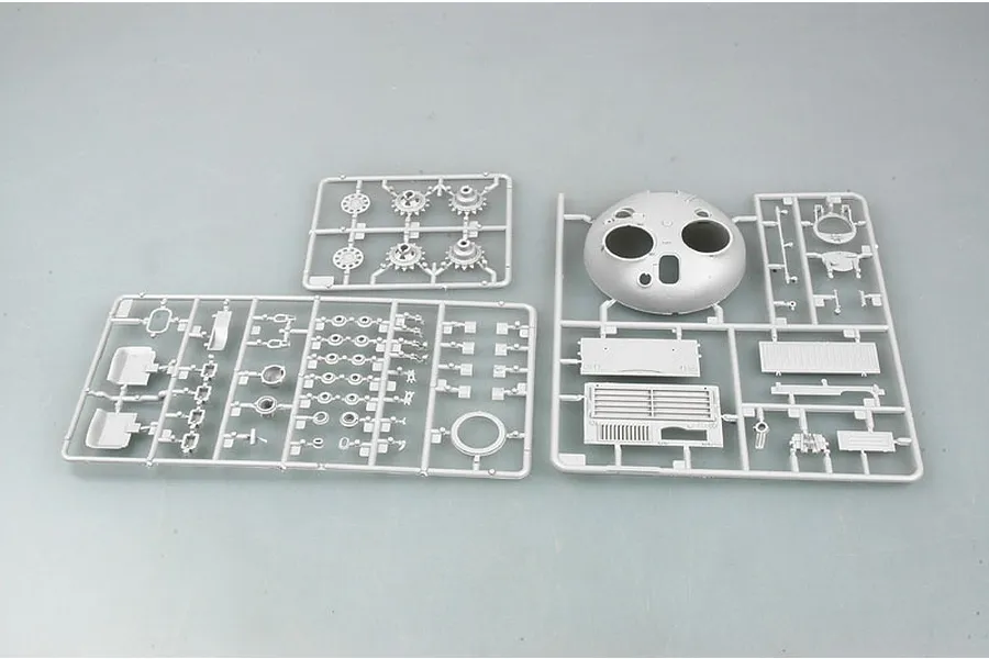 Three grey plastic model kit sprues containing tank parts, including a turret and various suspension components, on a plain background.