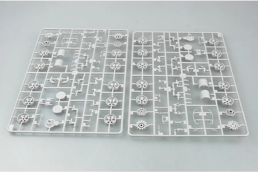 Two grey plastic model kit sprues containing tank road wheels and suspension parts on a light grey background.