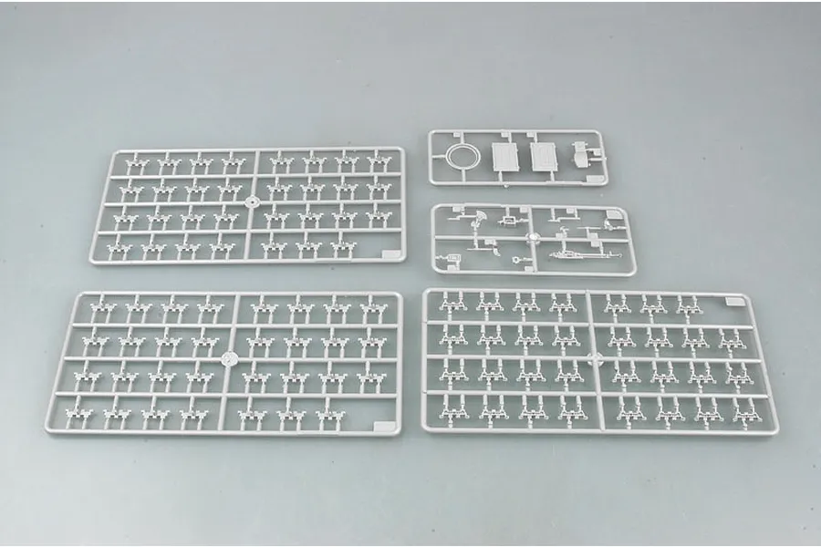 Four grey plastic model kit sprues containing various tank parts, including track links and small components, laid out on a plain grey background.
