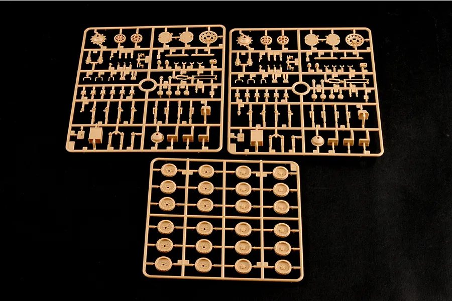 Three tan plastic model kit sprues containing various tank parts and road wheels on a black background.