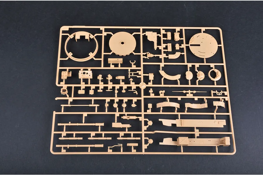 A tan plastic model kit sprue containing various tank parts, including circular turret components and gun barrels, laid out on a dark surface.