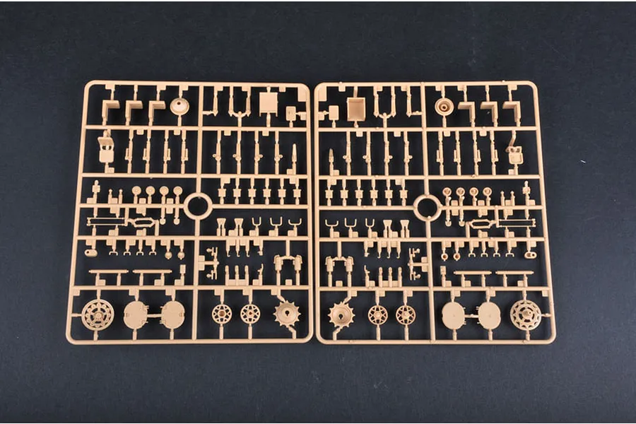 Two identical tan plastic model kit sprues showing various small tank parts, including wheels and structural components, against a dark background.