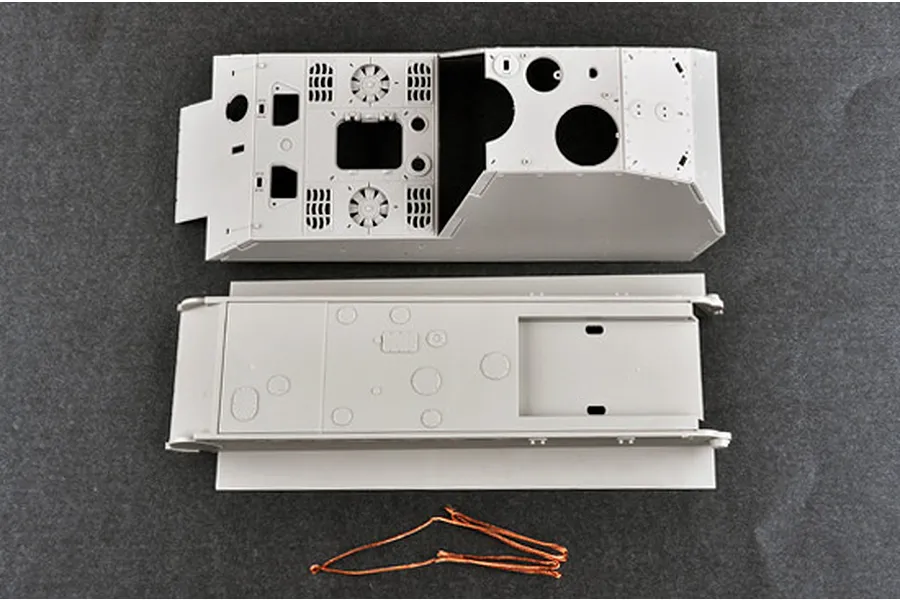 Top-down view of unpainted grey plastic model tank hull and upper chassis parts with a length of copper wire on a dark grey surface.