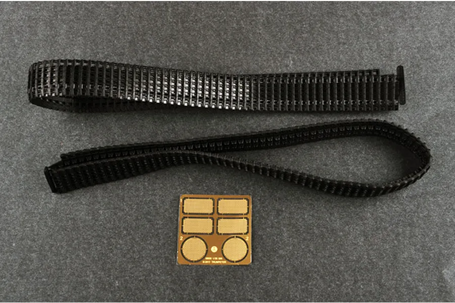 Two black plastic tank tracks and a small photo-etched brass detail sheet on a grey surface.