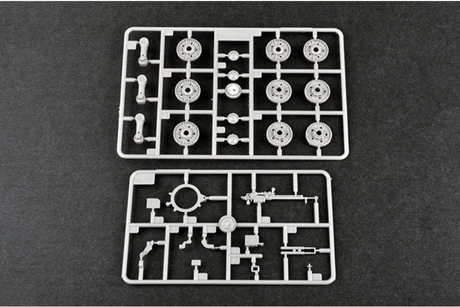 Two grey plastic model kit sprues containing tank wheels and small mechanical parts on a dark background.
