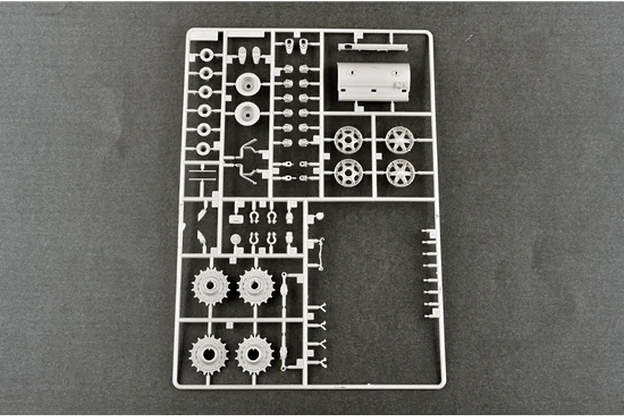 A grey plastic model kit sprue containing various tank parts, including wheels, sprockets, and structural components, on a dark grey background.