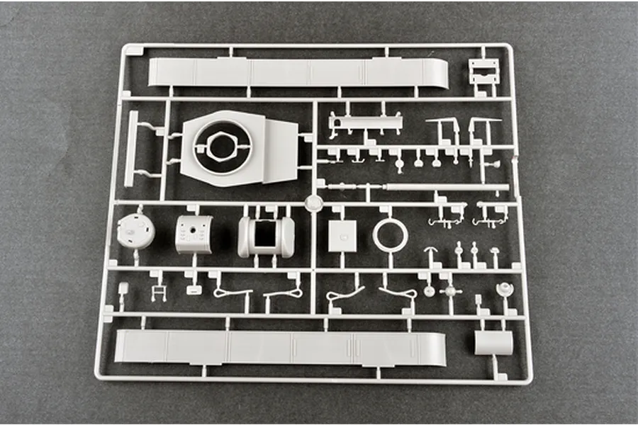 A grey plastic model kit sprue containing various tank parts, including turret components and side panels, on a dark grey background.
