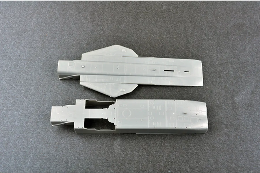 Two grey plastic model aircraft fuselage components from a Trumpeter 1/72 scale model kit laid out on a dark grey surface.
