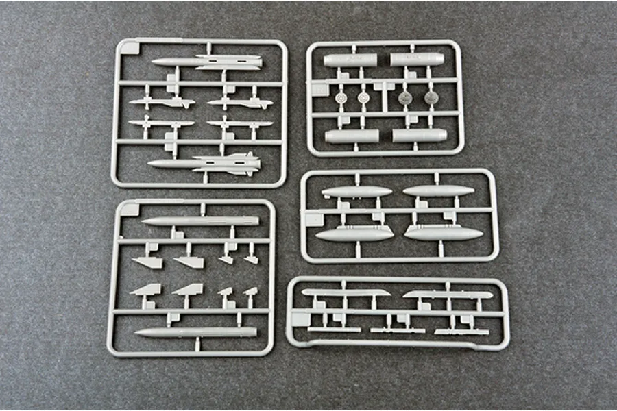 Five grey plastic model kit sprues containing various aircraft missiles, fuel tanks, and pylons on a dark grey background.