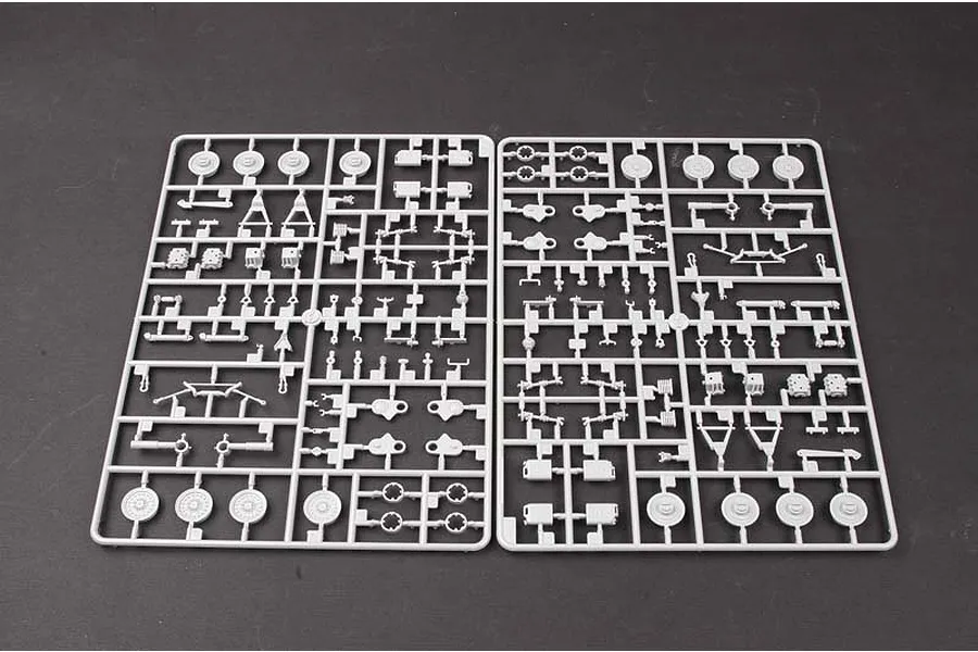 Two grey plastic model kit sprues containing various vehicle suspension and wheel parts laid out on a dark surface.