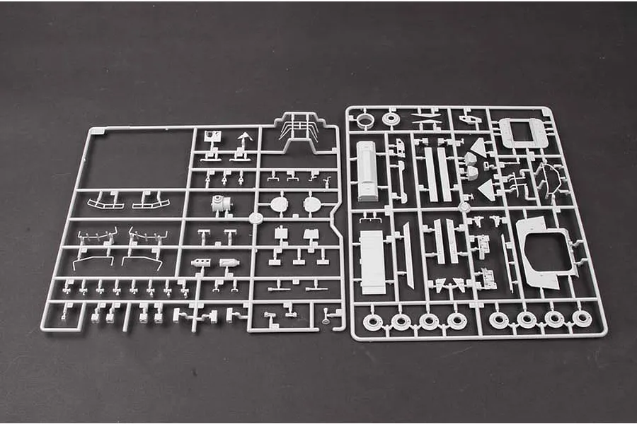 Two grey plastic model kit sprues containing various small vehicle parts laid out on a dark surface.