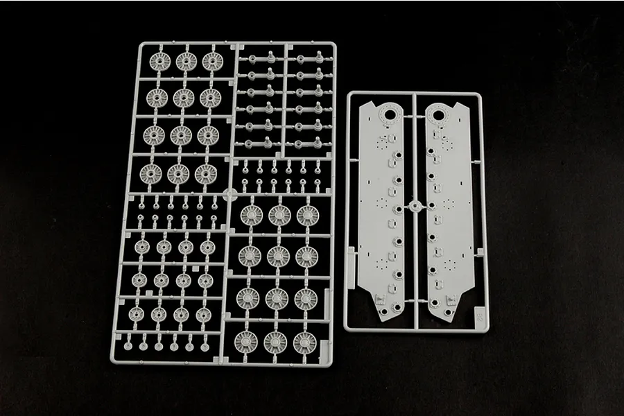 Two grey plastic model kit sprues containing tank road wheels and side hull panels on a black background.