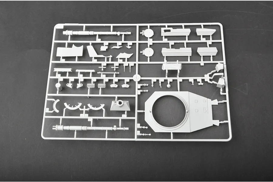 A light grey plastic model kit sprue containing various tank parts, including a turret ring and barrel, set against a dark grey background.