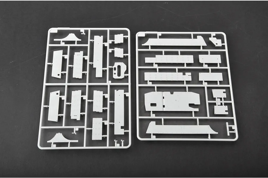 Two grey plastic model kit sprues containing various flat tank hull and armor plate parts laid out on a dark surface.