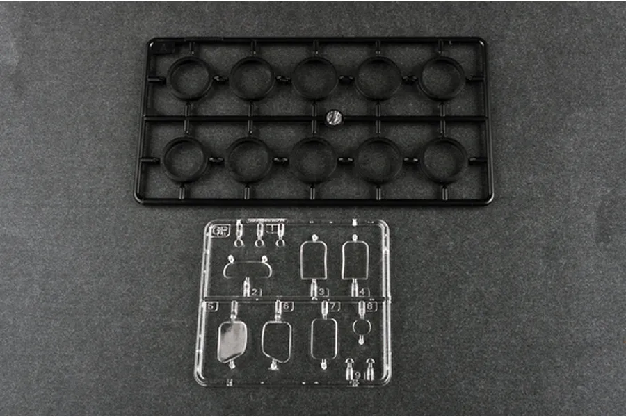Two plastic model kit sprues, one black with circular parts and one clear with various small rectangular and circular components.