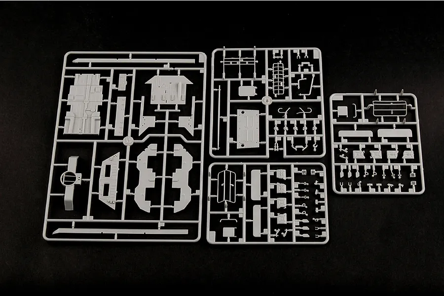 Three grey plastic model kit sprues containing various vehicle parts laid out on a black background.
