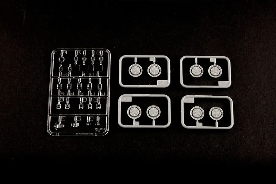 Plastic model kit sprues including one clear sprue and four grey sprues containing wheel parts on a black background.