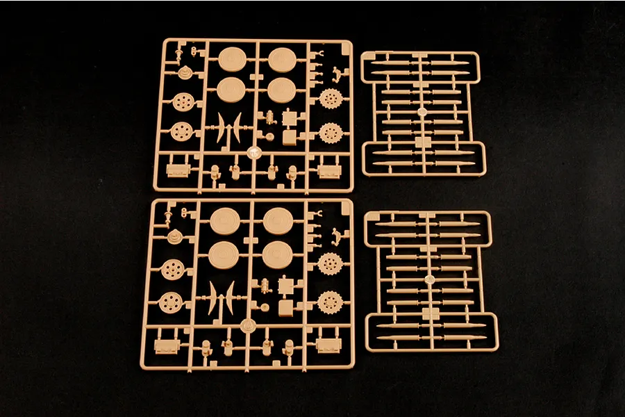 Four beige plastic model kit sprues containing tank wheels, sprockets, and ammunition shells on a black background.