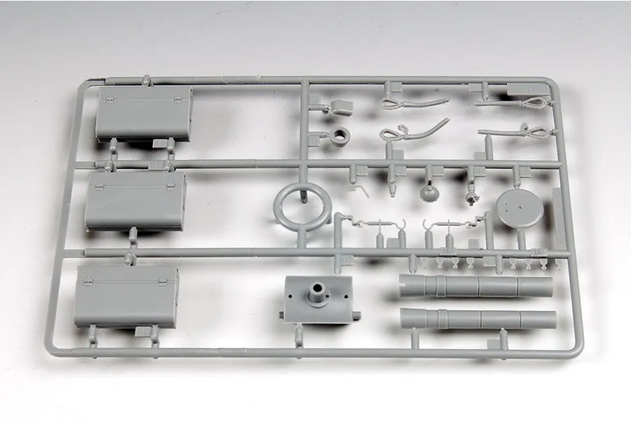 A grey plastic sprue containing various model tank parts, including storage boxes, cables, and cylindrical components, against a plain white background.