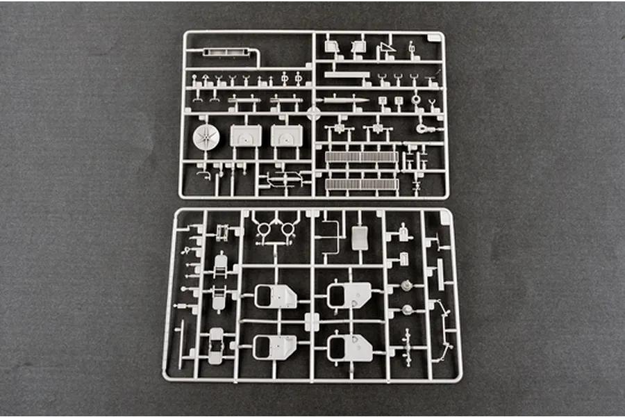 Two grey plastic model kit sprues containing various small vehicle parts laid out on a dark grey surface.