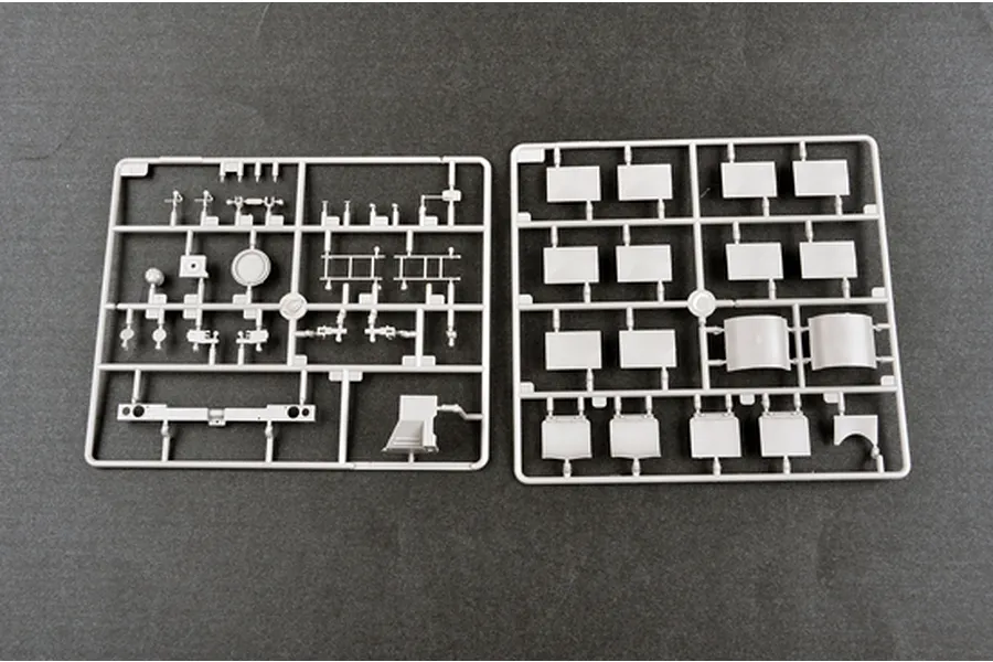 Two grey plastic model kit sprues containing various vehicle parts laid out on a dark grey surface.