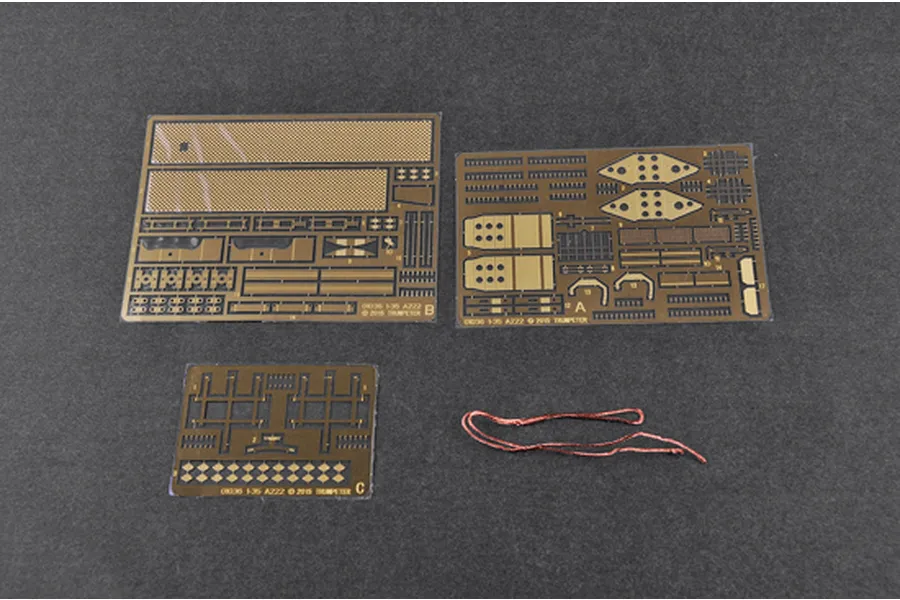 Three photo-etched metal detail sheets and a piece of copper wire for a 1/35 scale model kit on a dark grey surface.