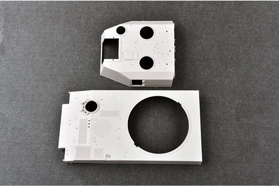 Top-down view of two unpainted light grey plastic model kit parts for a military vehicle, likely a turret and hull deck.