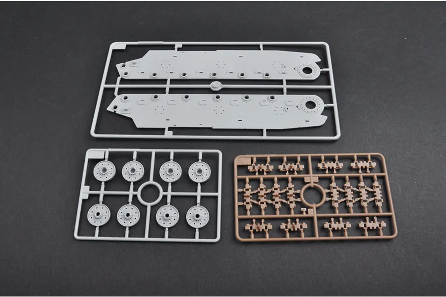 Three plastic model kit sprues on a dark grey background, including tank hull sides, road wheels, and track links.