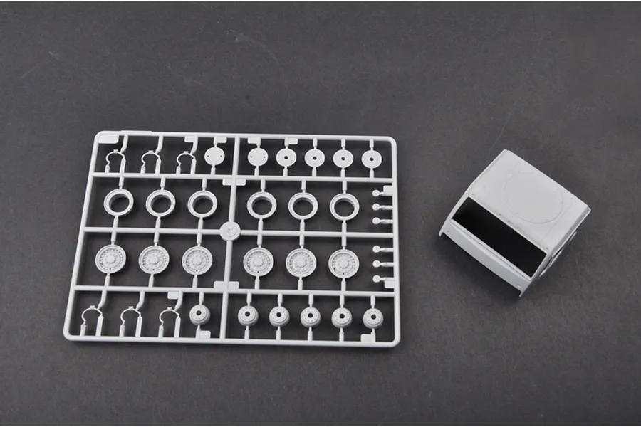 A grey plastic model kit sprue containing wheel and suspension parts alongside a separate truck cab component on a dark grey surface.