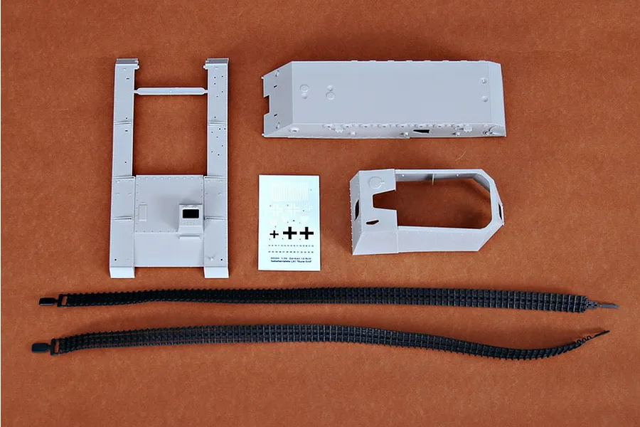 Plastic model kit parts for the Trumpeter 1/35 German 12.8cm Selbstfahrlafette, including hull sections, a decal sheet, and two black rubber tracks.