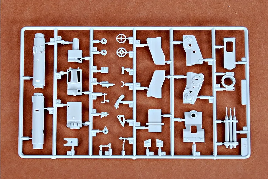 A grey plastic sprue containing various model kit parts for a 1/35 scale military vehicle, laid out on a brown surface.
