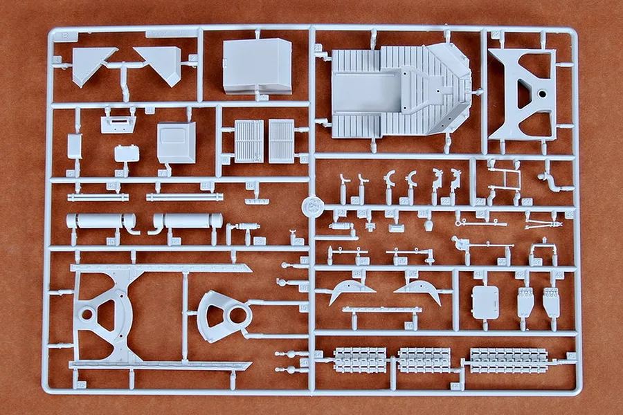 A grey plastic sprue containing various parts for a 1/35 scale military vehicle model kit, laid out on a brown surface.