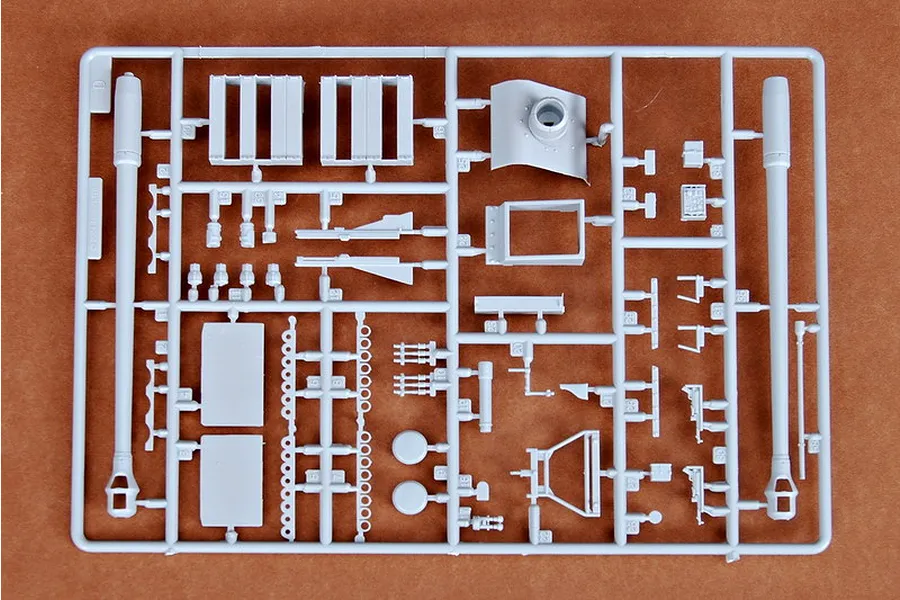 A grey plastic sprue containing various model kit parts for a 1/35 scale military vehicle, including long gun barrels and armor plates.