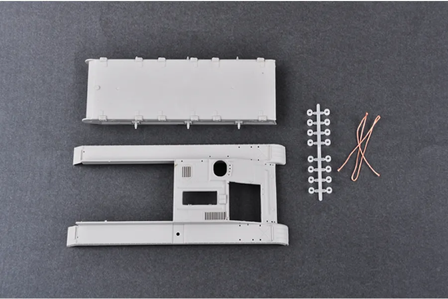 Unassembled plastic model kit parts including a tank hull, upper chassis, a small sprue of parts, and copper wire on a dark grey background.