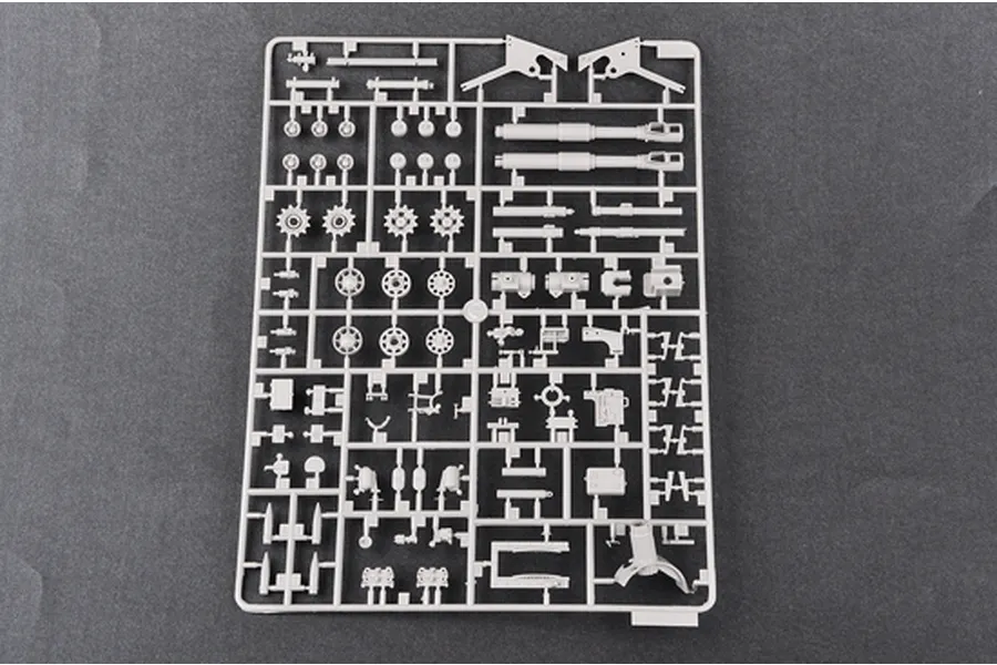 A grey plastic sprue containing various model kit parts for a military vehicle, including wheels, gun barrels, and structural components.