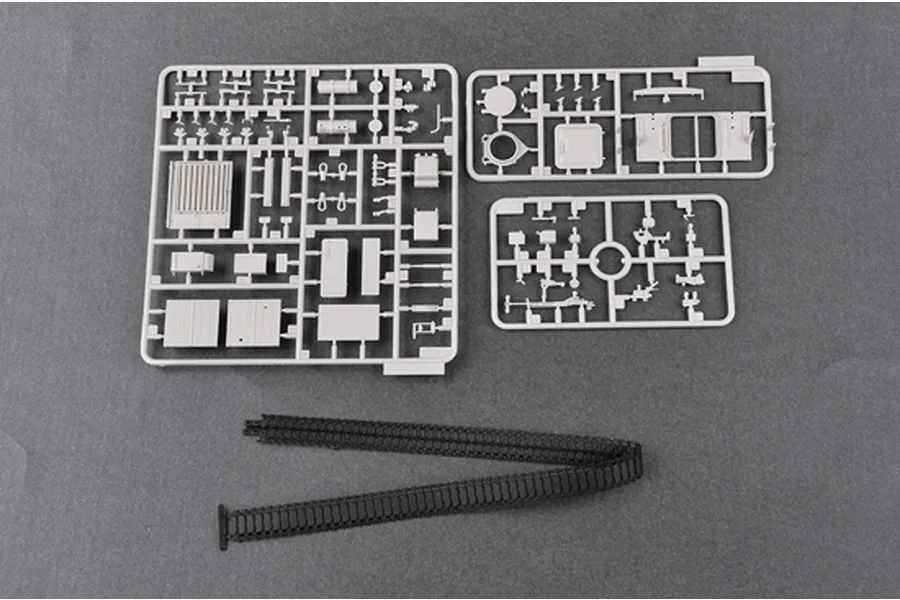 Three grey plastic model kit sprues and a pair of black rubber tank tracks laid out on a dark grey surface.