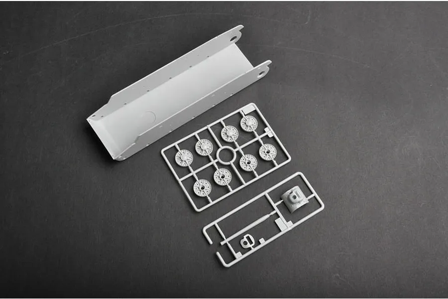 Plastic model tank parts including a hull tub and two sprues with wheels and small components on a dark grey surface.