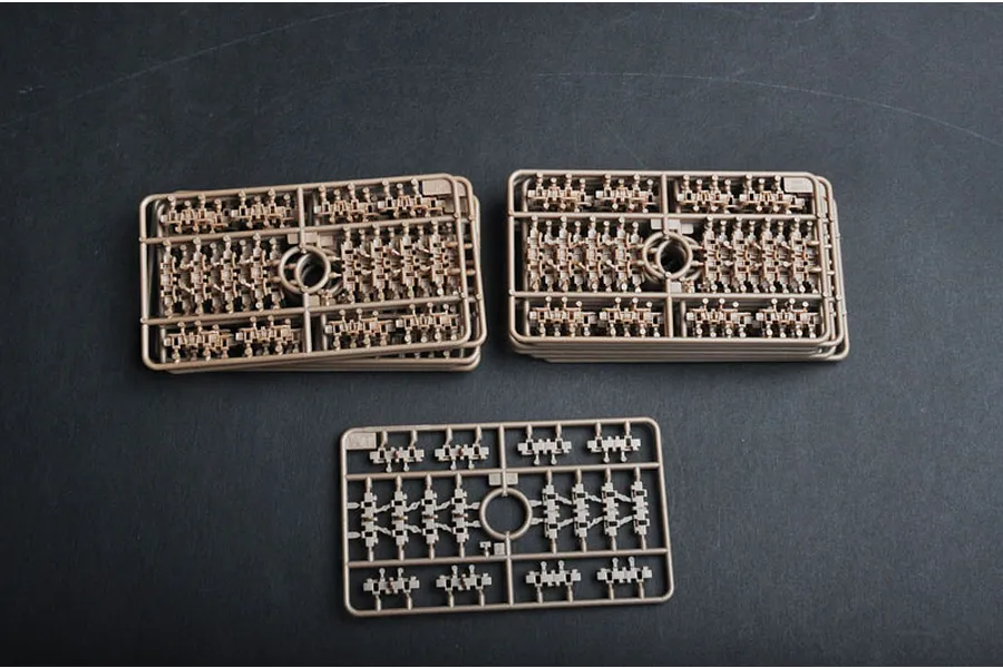 Three sprues of tan plastic tank track links for a 1/35 scale model kit, arranged on a dark surface.