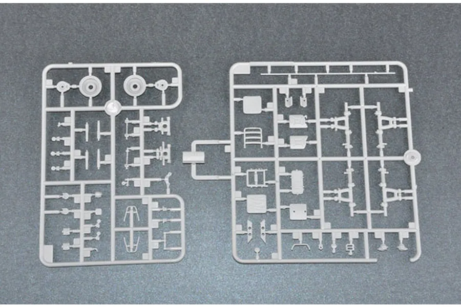Two grey plastic model kit sprues containing various small vehicle parts laid out on a dark grey surface.