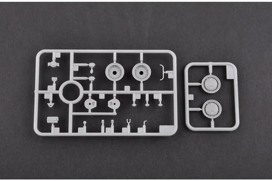 Two grey plastic model kit sprues containing various small vehicle parts and wheel components on a dark grey background.