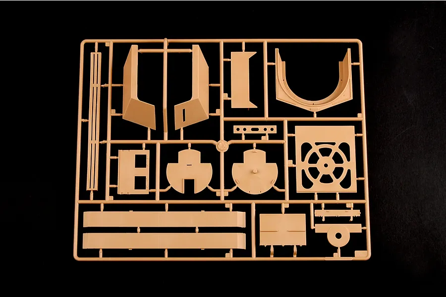 A tan plastic sprue containing various model kit parts for a military vehicle, set against a plain black background.