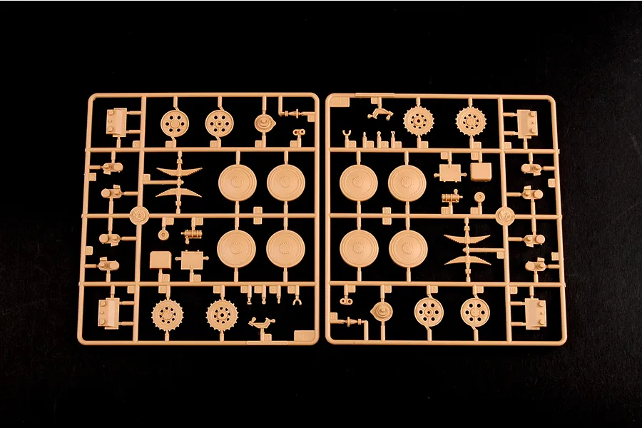 Two tan plastic model kit sprues containing various tank wheels, sprockets, and suspension parts on a black background.