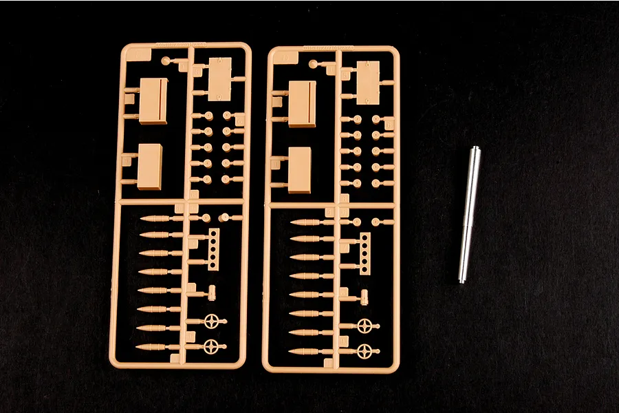 Two identical tan plastic model kit sprues and a single metal gun barrel component on a black background.