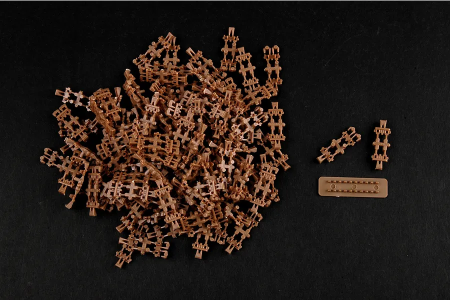 A pile of individual brown plastic tank track links for a 1/35 scale model kit on a black background.