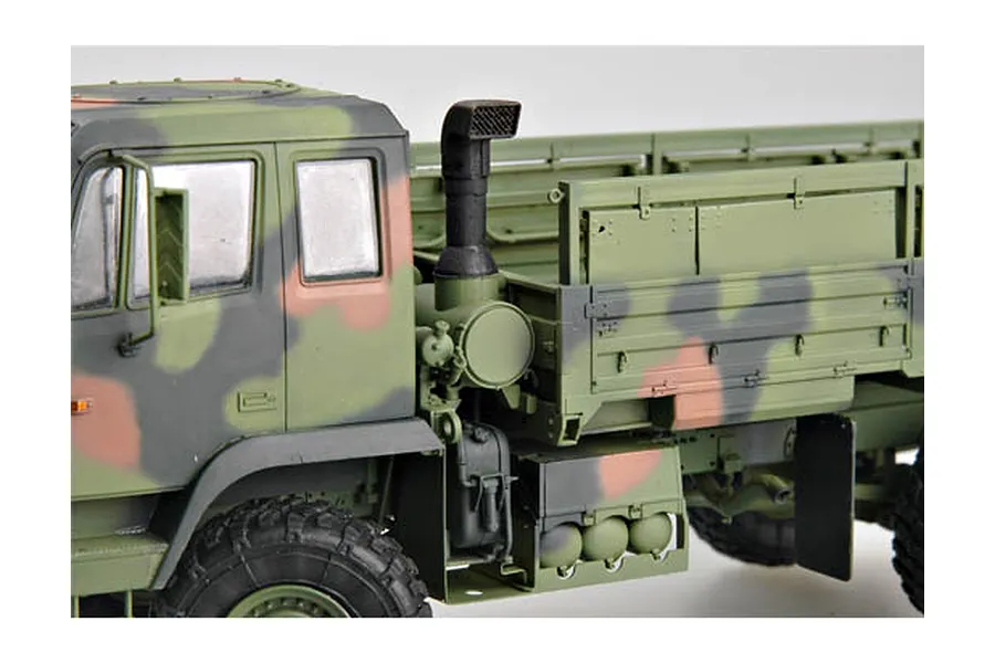 Close-up side view of a 1/35 scale model M1078 military cargo truck with camouflage paint, showing the cab, exhaust stack, and cargo bed.