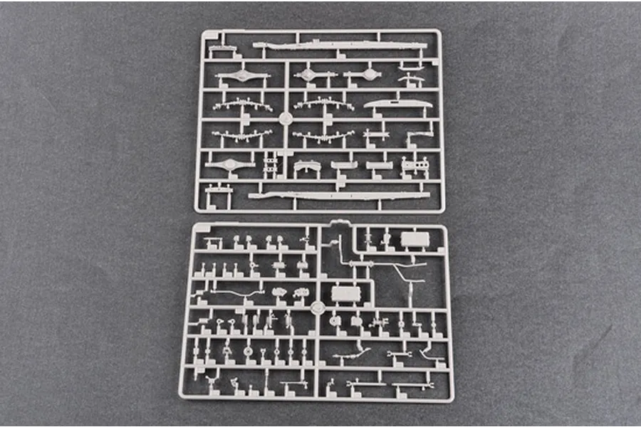 Two grey plastic model kit sprues containing various vehicle parts laid out on a dark grey surface.