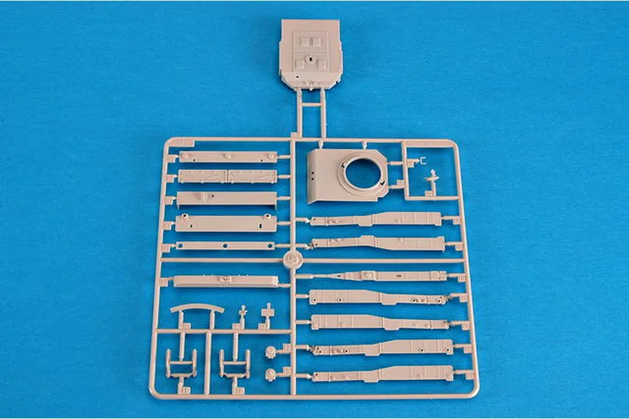 A beige plastic model kit sprue containing various vehicle parts for a 1/35 scale military model, set against a bright blue background.