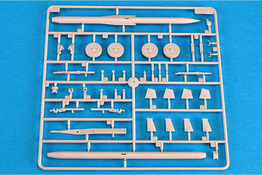 A plastic model kit sprue containing parts for a missile and wheels, laid out on a bright blue background.